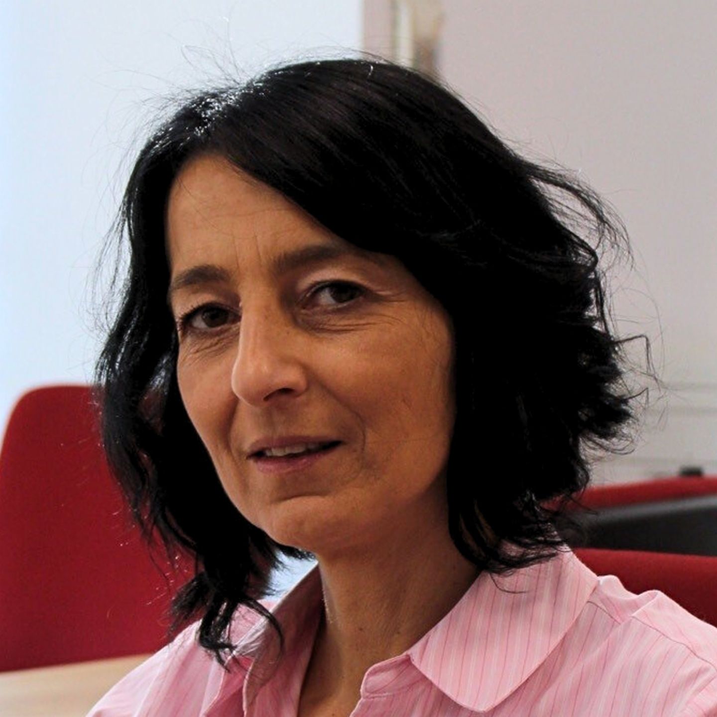 Η Cristina Pasere, Manager of Compliance Operations Support στην EOS Romania, κάθεται στο γραφείο της με μια ροζ ριγέ μπλούζα και κοιτάζει την κάμερα.