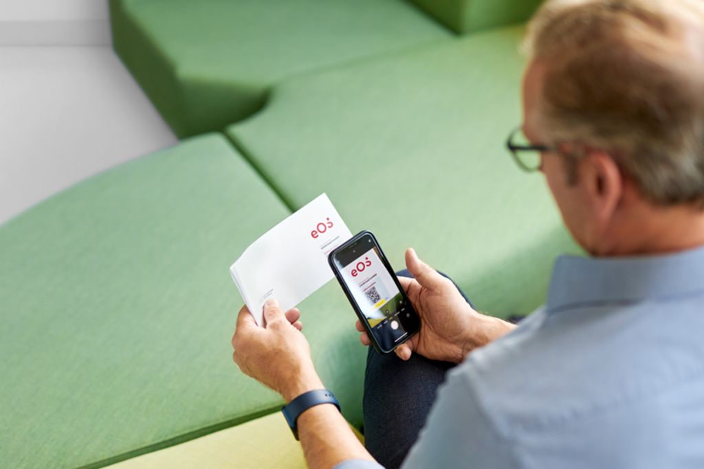 Ένας άντρας σκανάρει έναν QR κωδικό σε ένα γράμμα από την EOS με το smartphone του για να πληρώσει την εκκρεμή απαίτησή του online στην πύλη EOS.