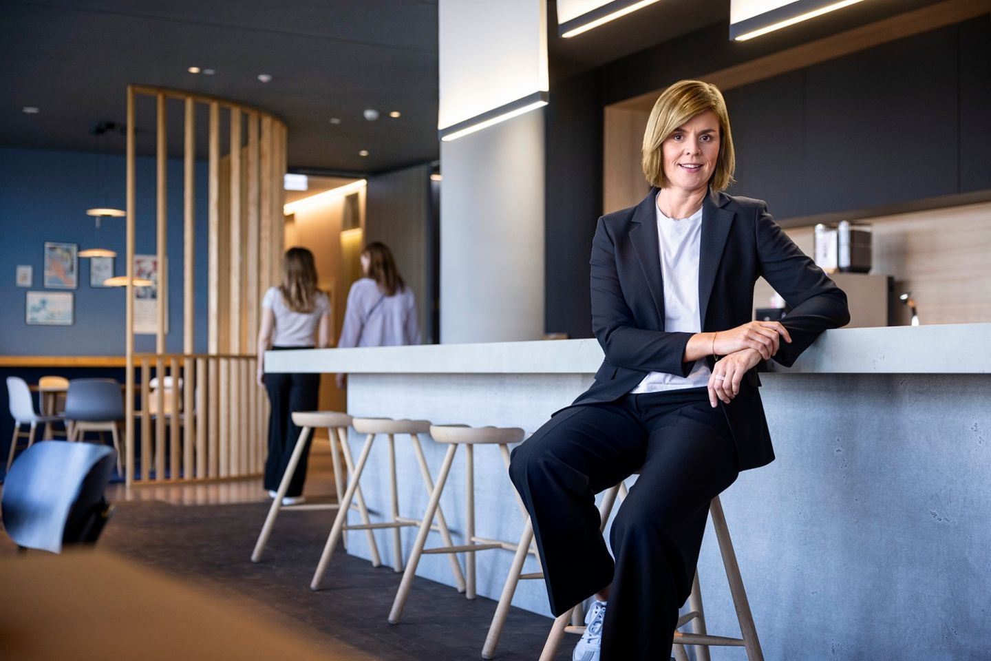 Η Δρ. Eva Griewel, CFO του Ομίλου EOS, κάθεται σε έναν κοινωνικό χώρο σε ένα ψηλό σκαμπό, φορώντας ένα μαύρο σακάκι.