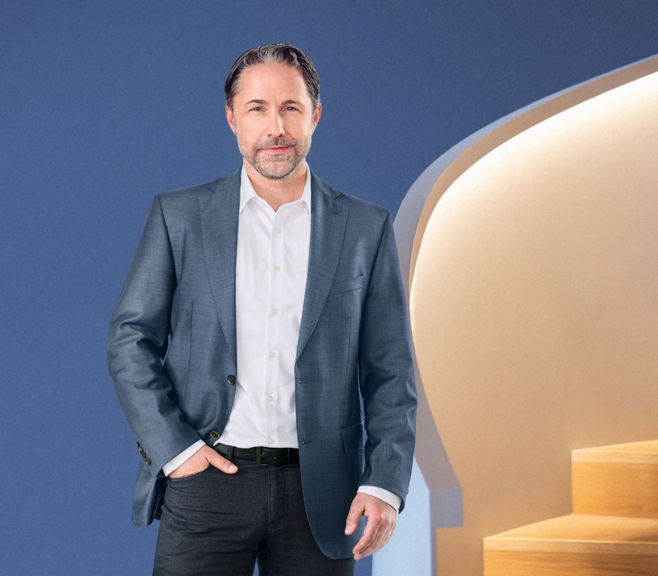 Ο Marwin Ramcke, Διευθύνων Σύμβουλος του ομίλου EOS, στέκεται μπροστά σε ένα μπλε φόντο, ντυμένος με ένα σκούρο σακάκι. Κοιτάζει απευθείας στην κάμερα.