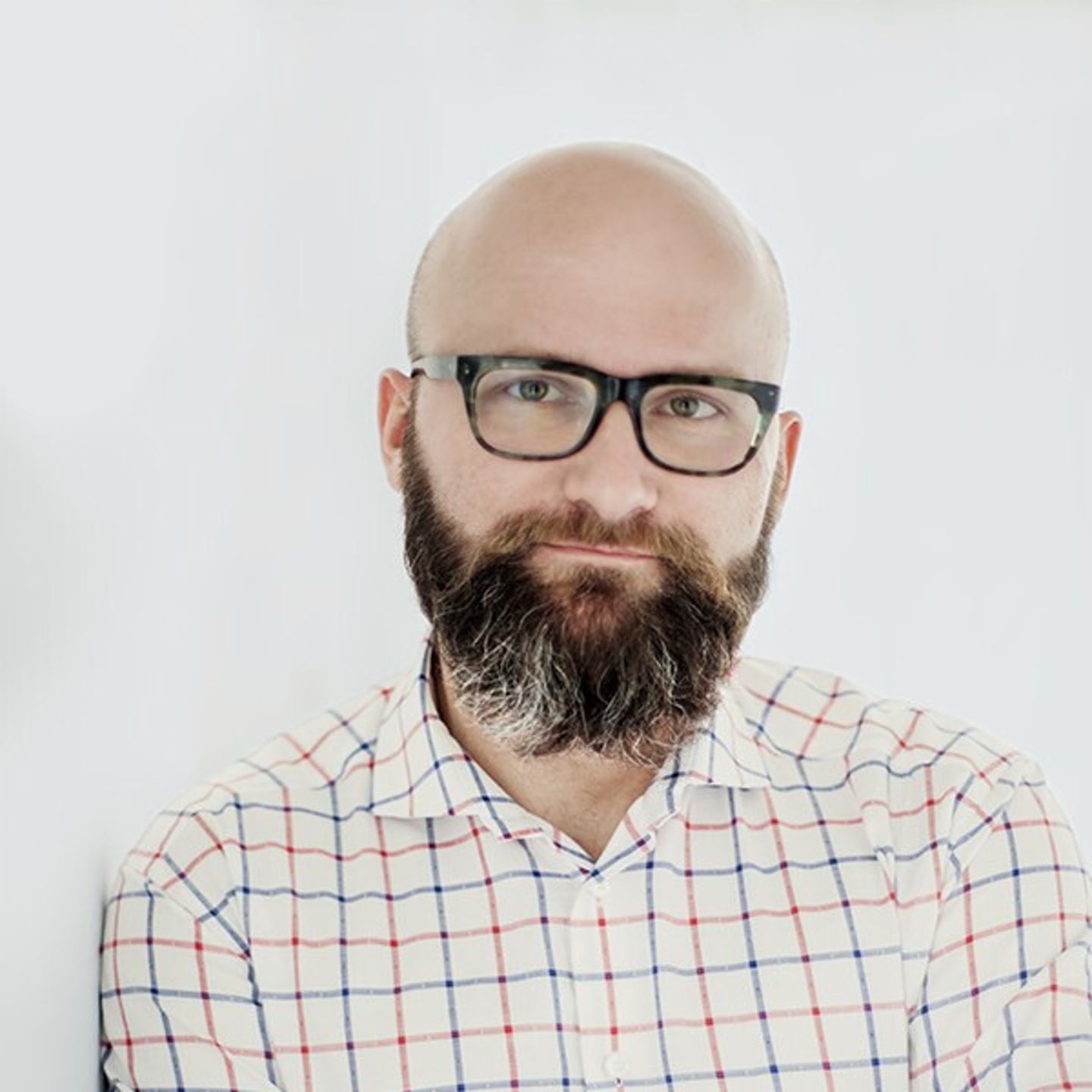 Dr hab. Tomasz Piekot Δρ. χ. Πιέκοτ με πουκάμισο καρό, ακουμπισμένος σε έναν λευκό τοίχο.