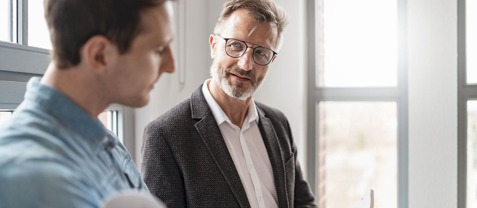 Δύο άνδρες σε ένα γραφείο ανταλλάσσουν ιδέες σχετικά με έγγραφα εργασίας για την ψηφιοποίηση.
