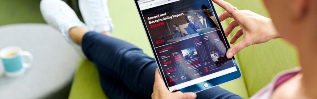Άτομο σε πράσινο καναπέ που προβάλλει την Ετήσια Έκθεση και Έκθεση Βιωσιμότητας της EOS 2024/25 σε tablet
