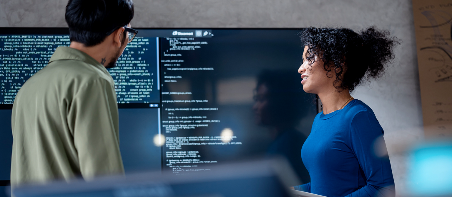 AI στην διαχείριση οφειλών: Σε αυτή την εικόνα, δύο επαγγελματίες αναλύουν συνεργατικά τον προγραμματισμένο κώδικα για αυτοματοποιημένες διαδικασίες σε μια μεγάλη οθόνη. Η σκηνή απεικονίζει την πρακτική εφαρμογή της Τεχνητής Νοημοσύνης (AI) και της Ρομποτικής Αυτοματοποίησης Διαδικασιών (RPA) στη διαχείριση χρεών – ένα παράδειγμα ψηφιακού μετασχηματισμού στη διαχείριση απαιτήσεων.